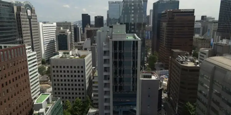 Vista aérea de un denso distrito urbano con numerosos rascacielos y edificios de oficinas modernos. Predominan estructuras de cristal y hormigón bajo un cielo parcialmente nublado, reflejando actividad económica.