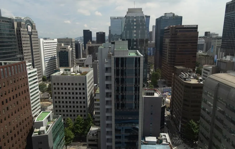 Vista aérea de un denso distrito urbano con numerosos rascacielos y edificios de oficinas modernos. Predominan estructuras de cristal y hormigón bajo un cielo parcialmente nublado, reflejando actividad económica.