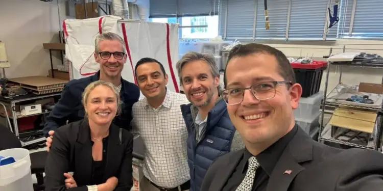 Un grupo de cinco profesionales sonrientes posando juntos en un espacio de trabajo de aspecto industrial.