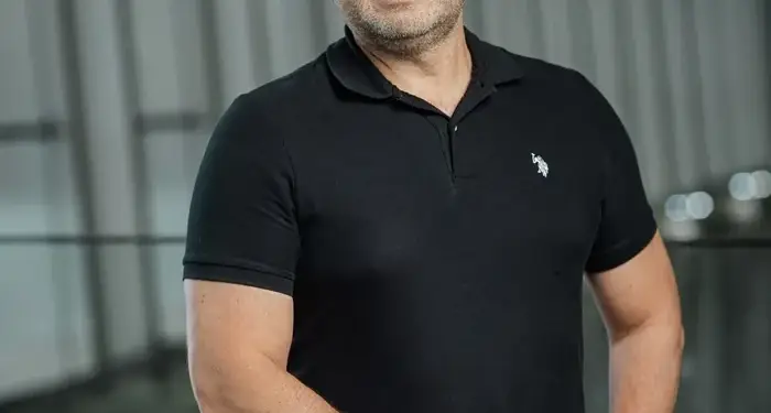 Hombre de mediana edad con gafas y camisa negra posando en una oficina moderna