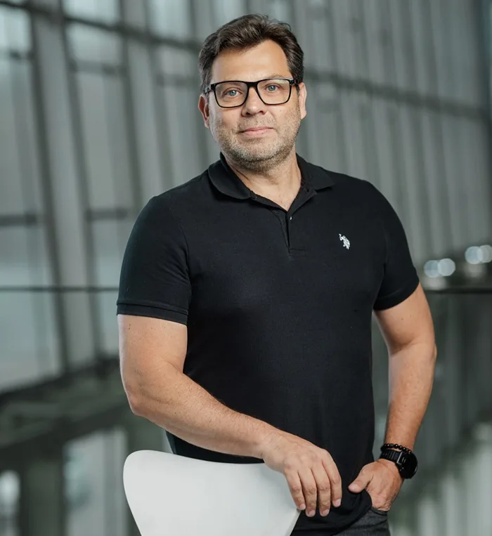 Hombre de mediana edad con gafas y camisa negra posando en una oficina moderna