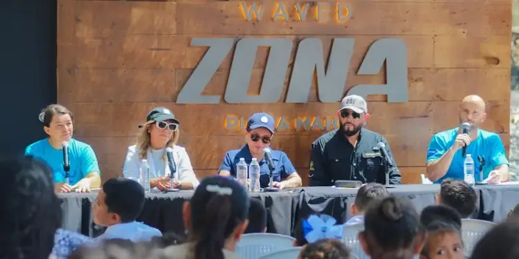 Cinco personas sentadas en un panel frente a una audiencia en un evento corporativo con pared de madera.