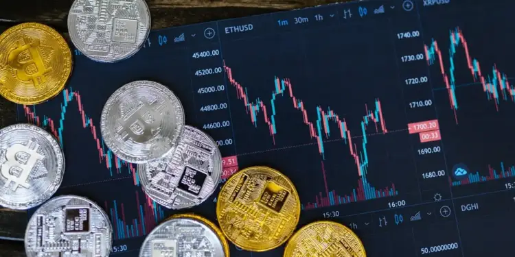 Monedas físicas de criptomonedas doradas y plateadas sobre una pantalla oscura con gráficos de trading bursátil.