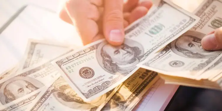 Primer plano de manos contando varios billetes de cien dólares estadounidenses, con enfoque en el retrato de Benjamin Franklin.