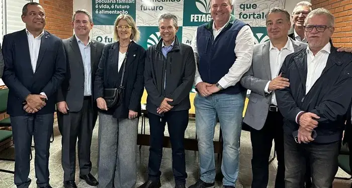 Grupo de hombres y una mujer de negocios posando juntos en una sala de reuniones con paneles informativos al fondo.