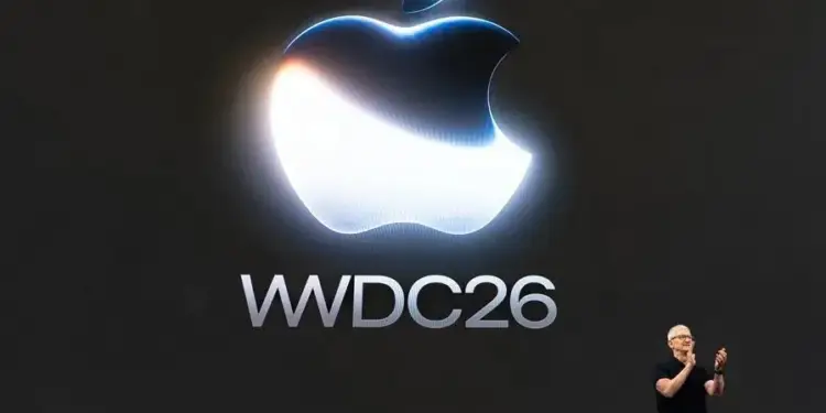 Presentador en el escenario frente a una gran pantalla oscura con el logotipo iluminado y el texto WWDC26.