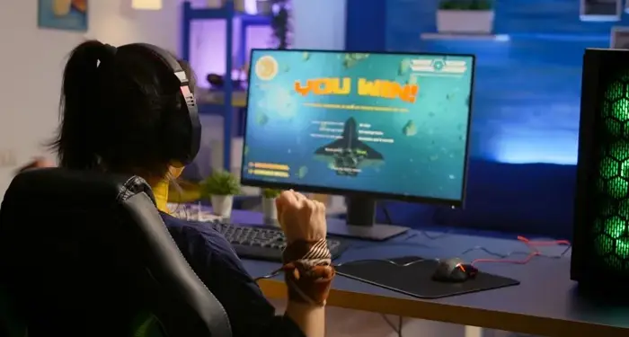 Una mujer con auriculares frente a un monitor de ordenador mostrando un mensaje de victoria.