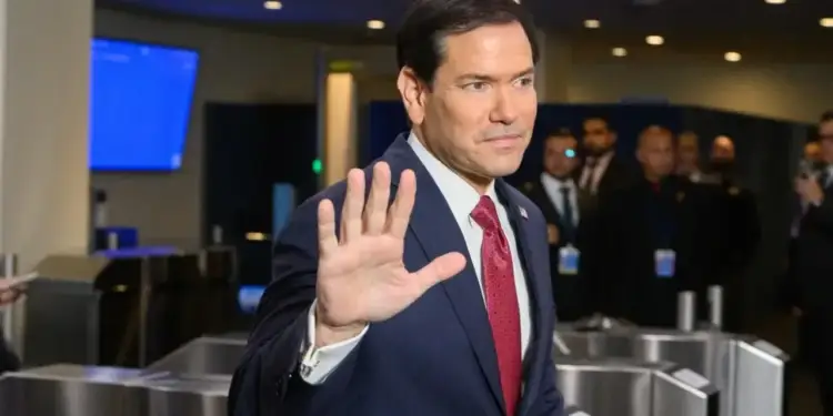 Hombre con traje azul y corbata roja levantando la mano en señal de saludo en un evento corporativo