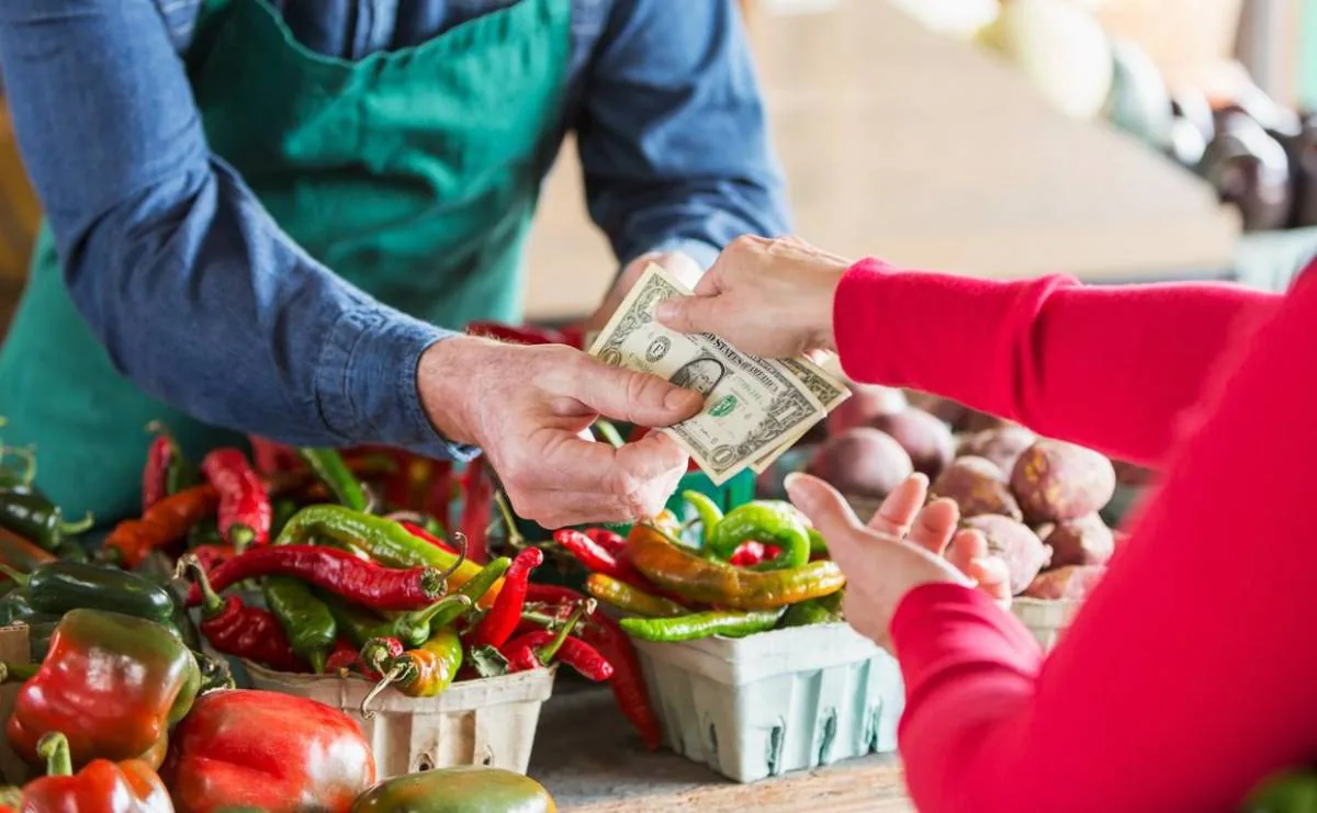 Cliente entregando billetes de dólares a un vendedor en un mercado de verduras