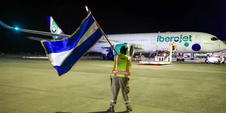Personal de tierra con bandera azul y blanca dirigiendo un avión Iberoject en pista de aeropuerto por la noche.