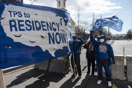 Grupo de manifestantes protestando con una pancarta azul que dice TPS to RESIDENCY NOW!