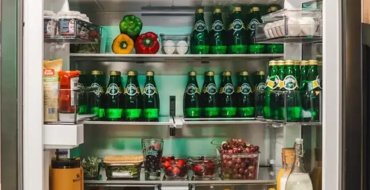 Refrigerador moderno con puertas francesas abiertas mostrando estantes organizados llenos de bebidas y alimentos frescos.