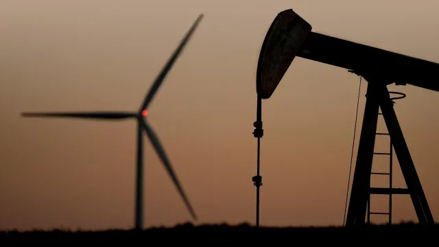 Silueta de una bomba de extracción de petróleo junto a un aerogenerador al atardecer, representando la transición energética.
