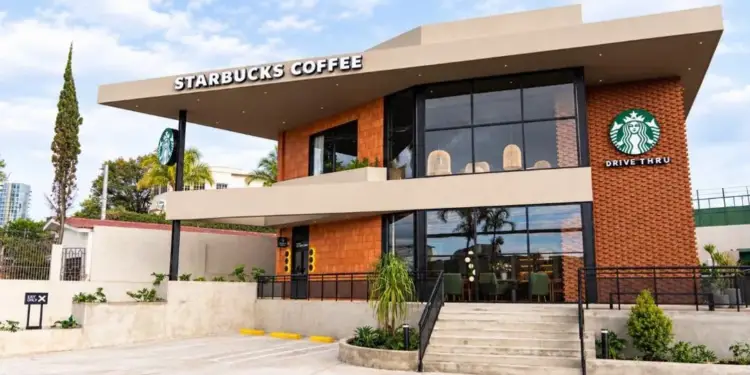 Fachada moderna de una cafetería Starbucks de dos pisos con servicio Drive Thru, grandes ventanales y detalles en ladrillo.