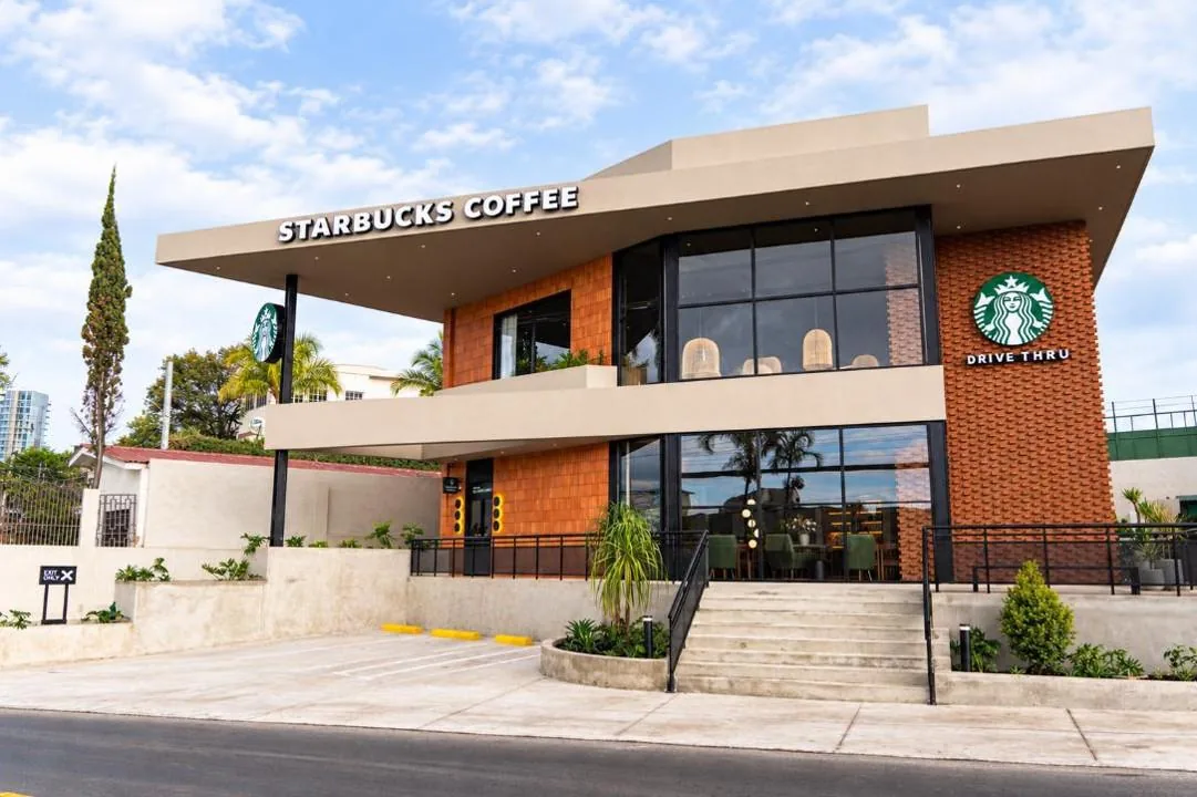 Fachada moderna de una cafetería Starbucks de dos pisos con servicio Drive Thru, grandes ventanales y detalles en ladrillo.