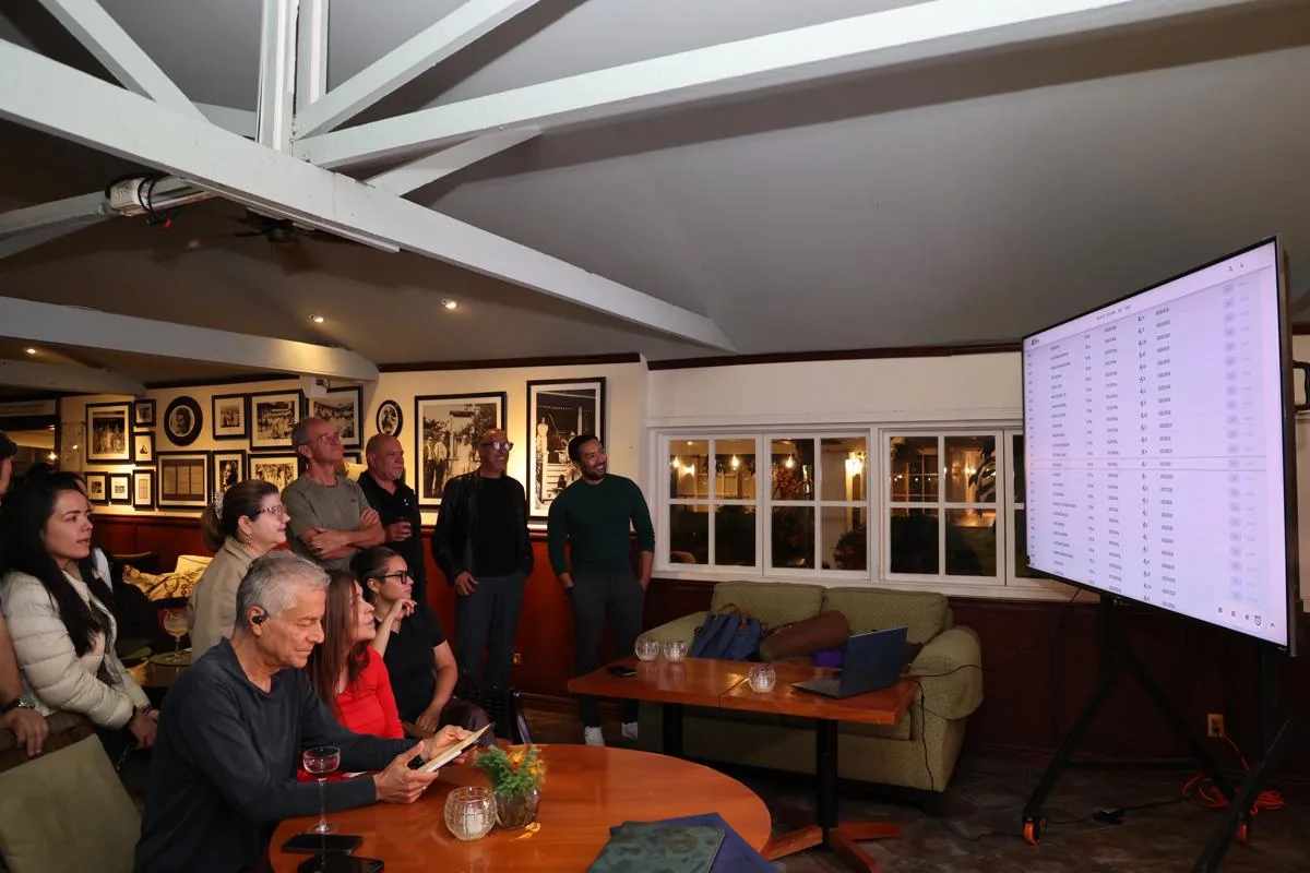 Un grupo de personas atentas mirando una pantalla grande con datos financieros en un espacio interior.