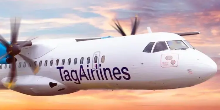 Avión turbopropulsor blanco de Tag Airlines volando al atardecer. Hélices azules y cielo con nubes rosadas y naranjas. Transporte aéreo y logística.
