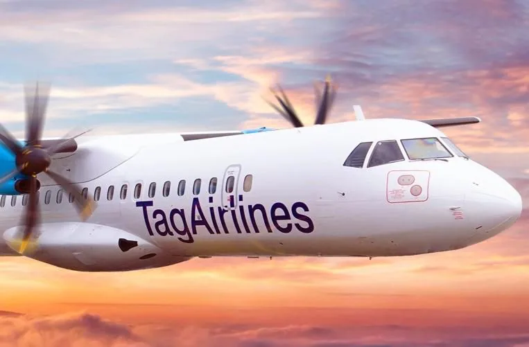 Avión turbopropulsor blanco de Tag Airlines volando al atardecer. Hélices azules y cielo con nubes rosadas y naranjas. Transporte aéreo y logística.