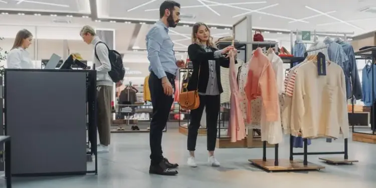 Pareja de clientes mirando ropa colgada en percheros dentro de una tienda