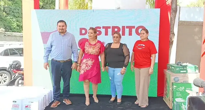 Cuatro personas de pie posando frente a un panel publicitario con la palabra Distrito.