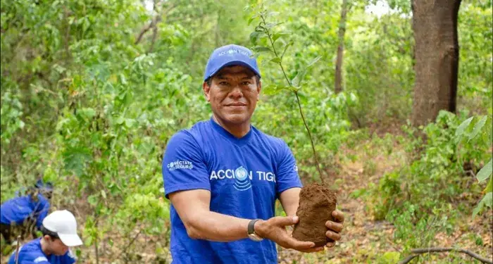 Hombre sosteniendo un árbol pequeño con tierra en sus manos durante una actividad de reforestación al aire libre
