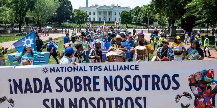 Grupo de personas manifestándose frente a un edificio gubernamental sosteniendo una pancarta con el texto National TPS Alliance.