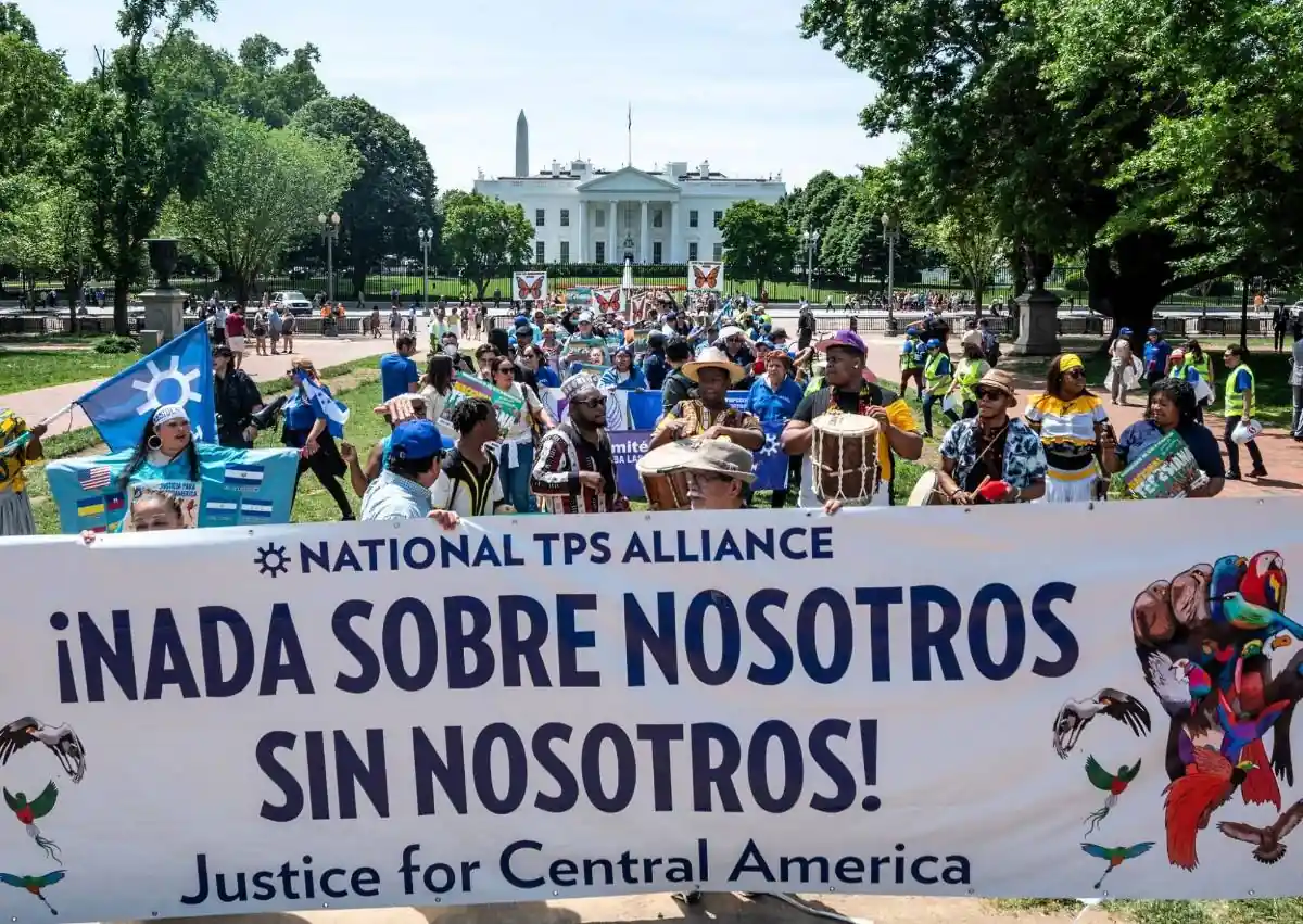Grupo de personas manifestándose frente a un edificio gubernamental sosteniendo una pancarta con el texto National TPS Alliance.