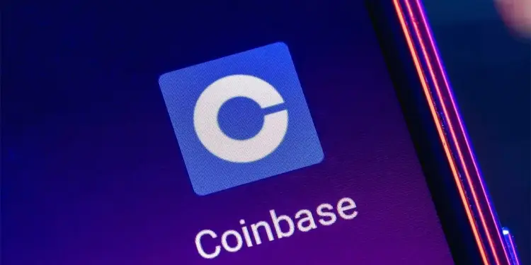 Primer plano del icono de la aplicación Coinbase con una 'C' blanca en un cuadrado azul, y el texto 'Coinbase' en una pantalla de smartphone. Fondo morado con reflejos de luz.