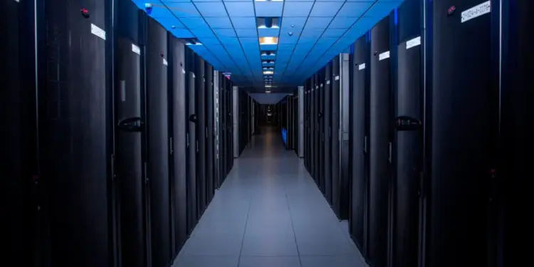 Pasillo iluminado con luz azul entre filas de gabinetes de servidores en un centro de datos moderno.