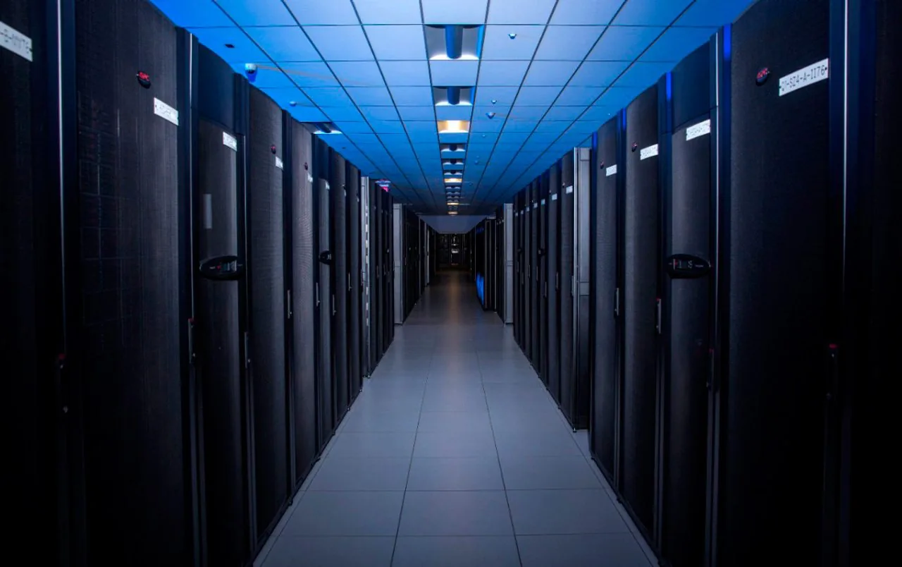 Pasillo iluminado con luz azul entre filas de gabinetes de servidores en un centro de datos moderno.