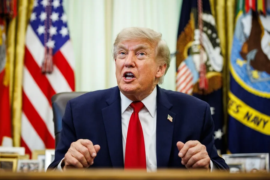 Donald Trump hablando frente a banderas estadounidenses en un despacho oficial.