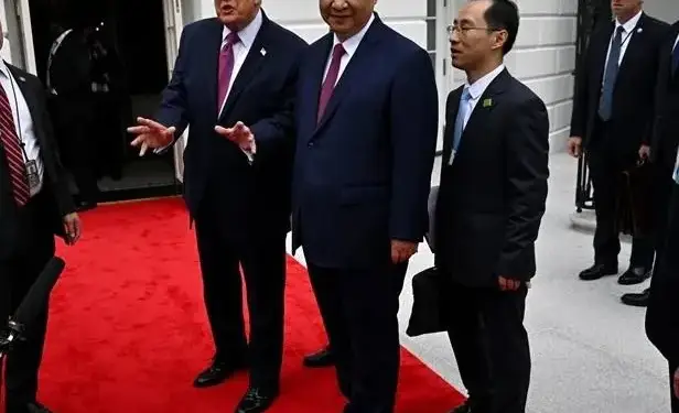 Dos líderes políticos con traje y corbata caminando sobre una alfombra roja junto a otros oficiales.