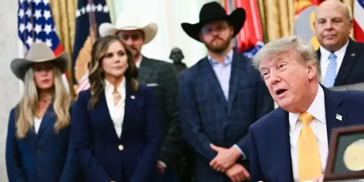 Un hombre con traje azul y corbata amarilla hablando ante varias personas con sombreros de vaquero.