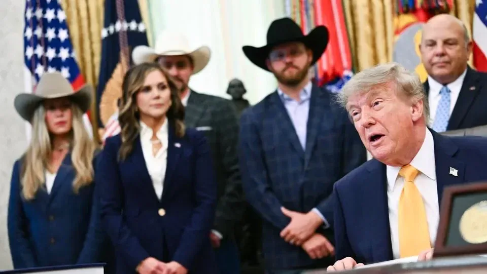 Un hombre con traje azul y corbata amarilla hablando ante varias personas con sombreros de vaquero.