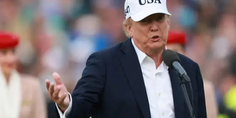 Hombre de negocios hablando ante un micrófono con traje oscuro y gorra blanca con el texto USA.