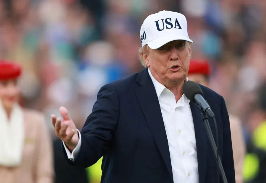 Hombre de negocios hablando ante un micrófono con traje oscuro y gorra blanca con el texto USA.