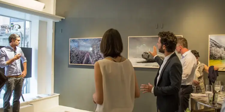 Grupo de profesionales observando y discutiendo sobre obras de arte en una galería con paredes oscuras.