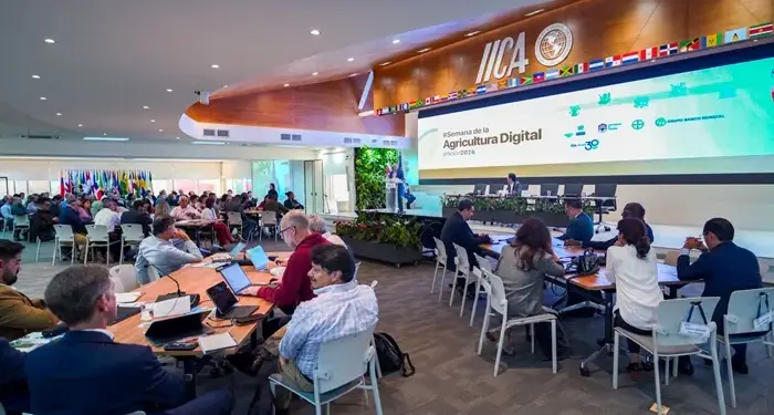 Vista general de una conferencia sobre agricultura digital. Numerosos profesionales asisten, con un orador en el escenario y una pantalla mostrando el título del evento y logos como IICA y Grupo Banco Mundial.