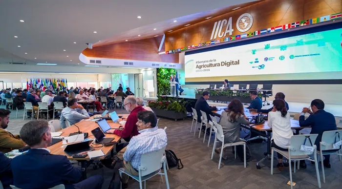 Vista general de una conferencia sobre agricultura digital. Numerosos profesionales asisten, con un orador en el escenario y una pantalla mostrando el título del evento y logos como IICA y Grupo Banco Mundial.