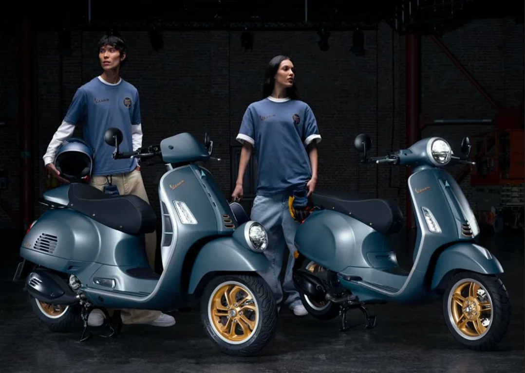 Hombre y mujer de pie en un estudio oscuro junto a dos motocicletas azules con detalles dorados.