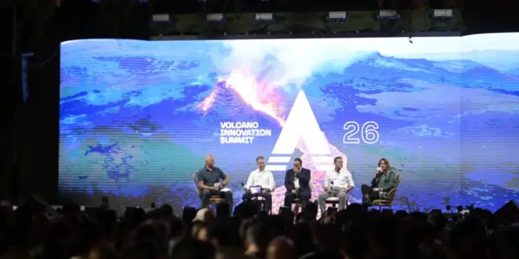 Cinco personas sentadas en un escenario frente a una gran pantalla con un público asistente en un evento de negocios.