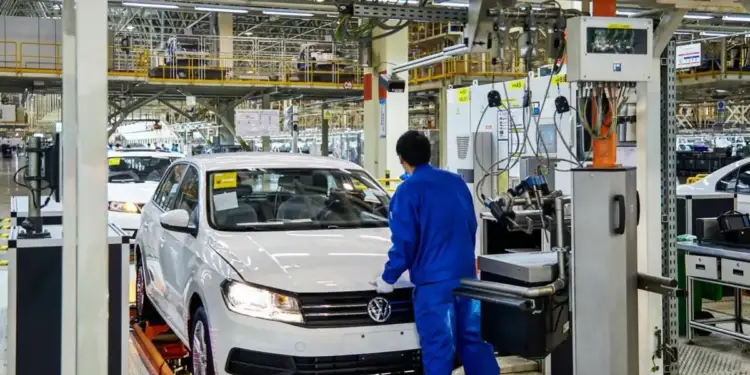 Operario con uniforme azul inspecciona un automóvil blanco en una línea de montaje e inspección industrial.