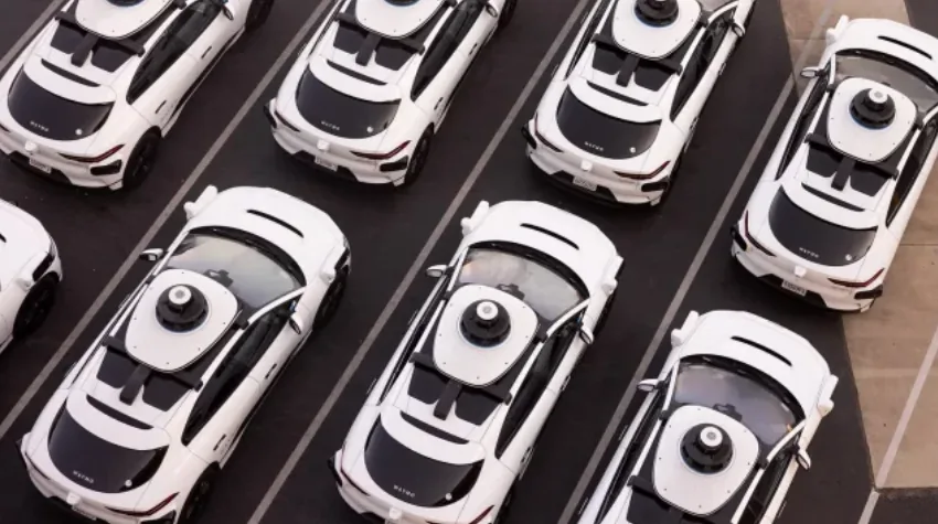 Vista aérea de varios automóviles blancos con equipos de sensores en el techo estacionados ordenadamente.