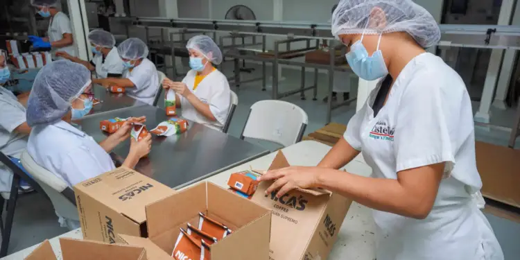 Operarias con cofia y mascarilla empacan sobres de café Nica's en cajas en la planta de Cafetalera Castellón