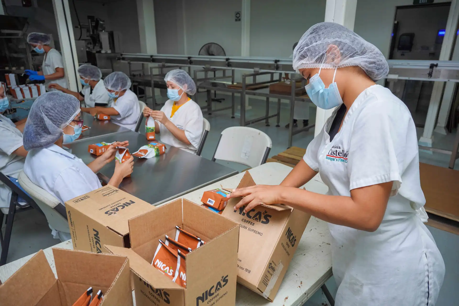 Operarias con cofia y mascarilla empacan sobres de café Nica's en cajas en la planta de Cafetalera Castellón