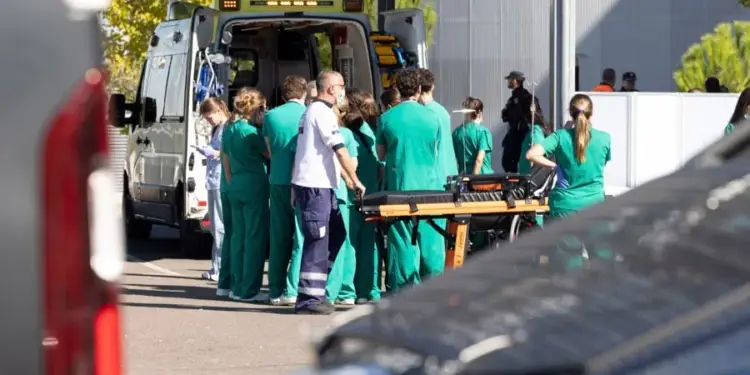 Grupo de profesionales de la salud con uniformes verdes y un paramédico junto a una ambulancia con puertas abiertas y una camilla. Escena de emergencia médica al aire libre.