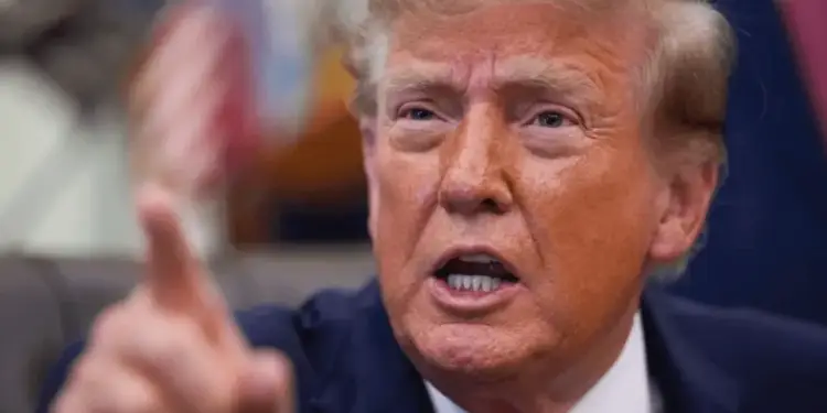 Primer plano de un hombre con cabello rubio, traje oscuro y corbata roja, señalando con el dedo índice derecho y hablando con intensidad.