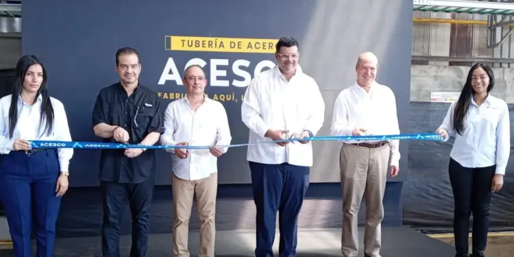 Seis personas, cuatro hombres y dos mujeres, cortan una cinta azul en una ceremonia de inauguración de una planta industrial de tubería de acero.