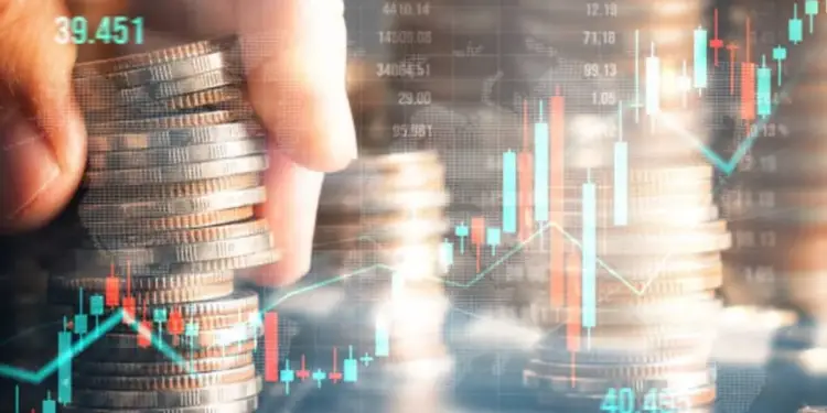 Mano apilando monedas de diferentes metales sobre un fondo de gráficos bursátiles y datos financieros digitales, simbolizando inversión y crecimiento económico.