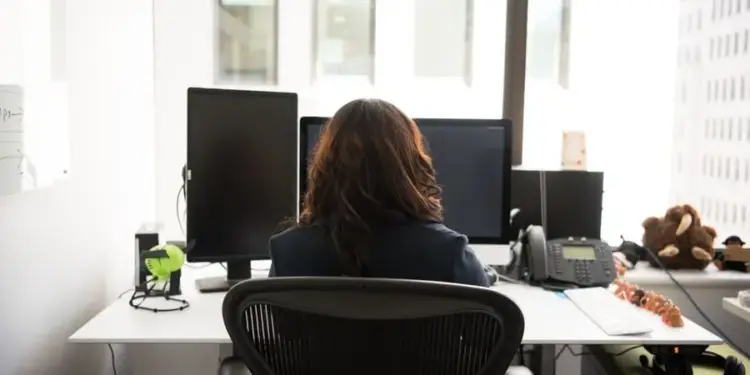 Vista trasera de una mujer trabajando en su escritorio de oficina con doble monitor y ordenador